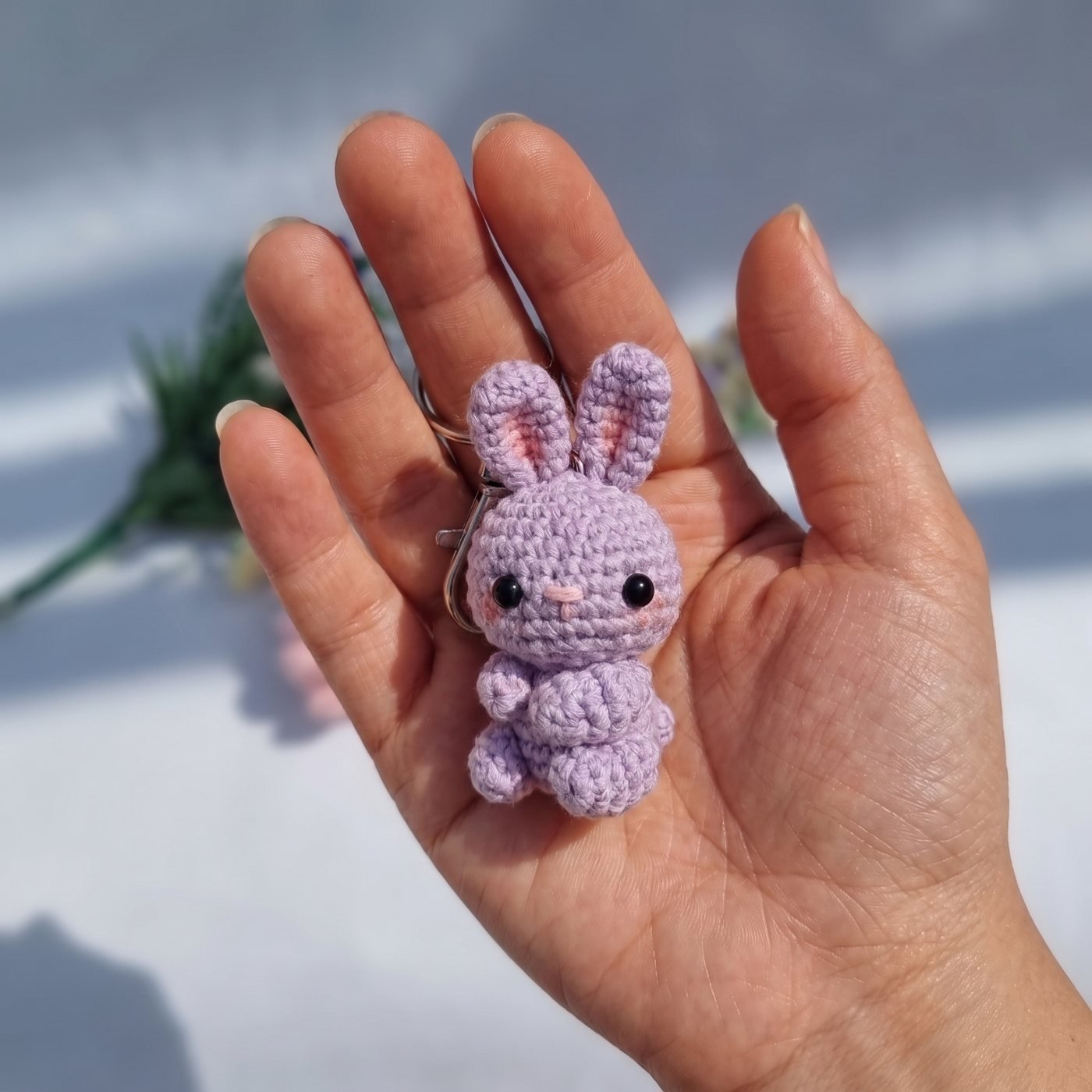 Lila gehäkelter Mini-Hase mit rosa Innenohren und Wangen auf einer offenen Handfläche